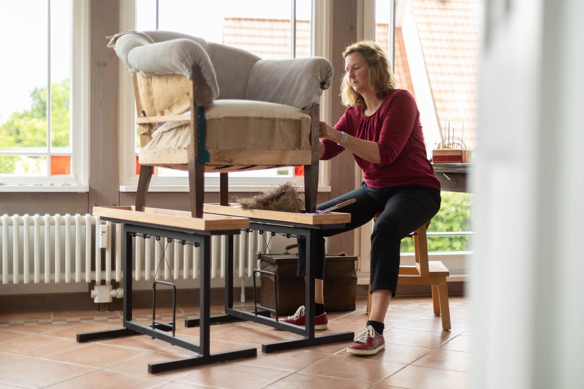 Eine Frau sitzt auf einer Bank und arbeitet an einem Stuhl.