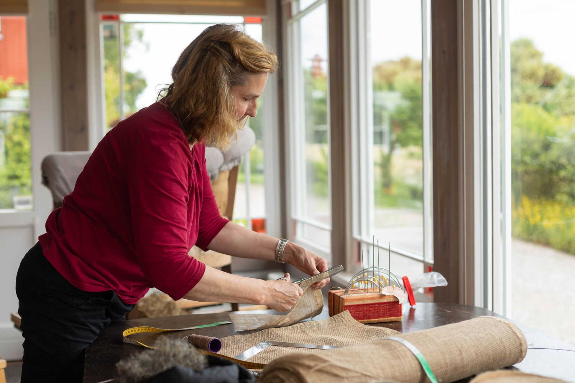 Eine Frau schneidet auf einem Tisch vor einem Fenster ein Stück Stoff zu.