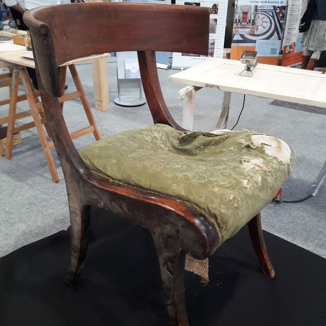 Ein Holzstuhl mit einem grünen Kissen steht auf einer schwarzen Matte