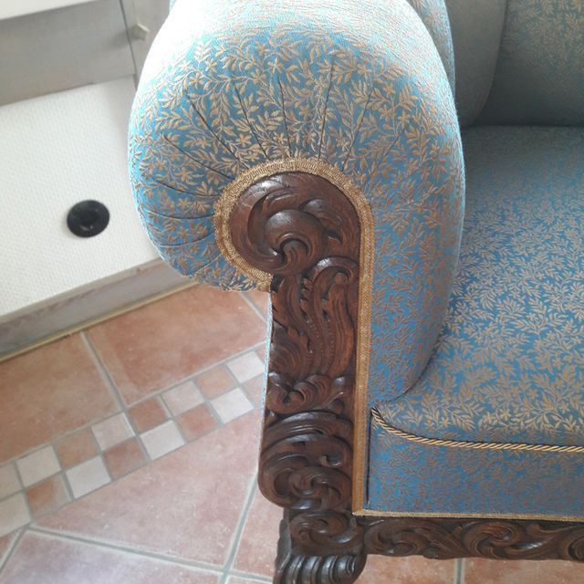 Auf einem gefliesten Boden steht ein blauer Stuhl mit Armlehnen aus Holz.