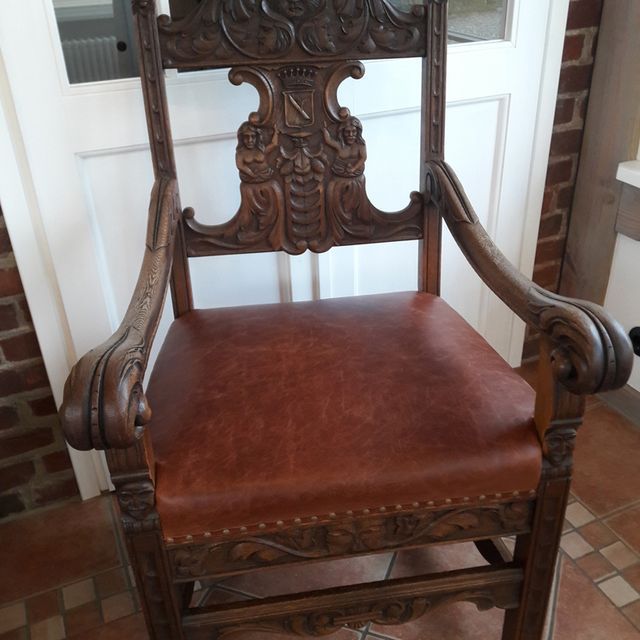 Ein geschnitzter Holzstuhl mit einem braunen Ledersitz