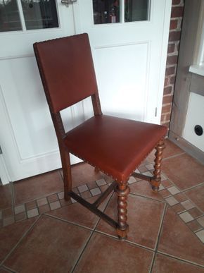 Ein Holzstuhl mit braunem Ledersitz steht auf einem gefliesten Boden vor einer Tür.