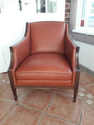 In einem Zimmer steht ein brauner Ledersessel auf einem gefliesten Boden.