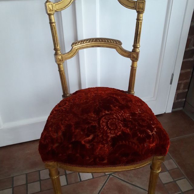 Ein goldener Stuhl mit einem roten Kissen steht vor einer weißen Tür