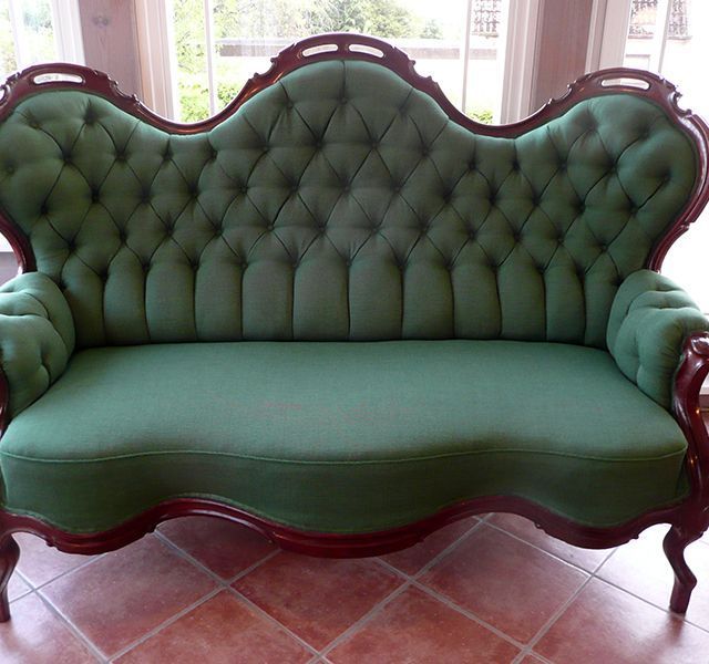 Eine grüne Couch steht auf einem gefliesten Boden vor einem Fenster