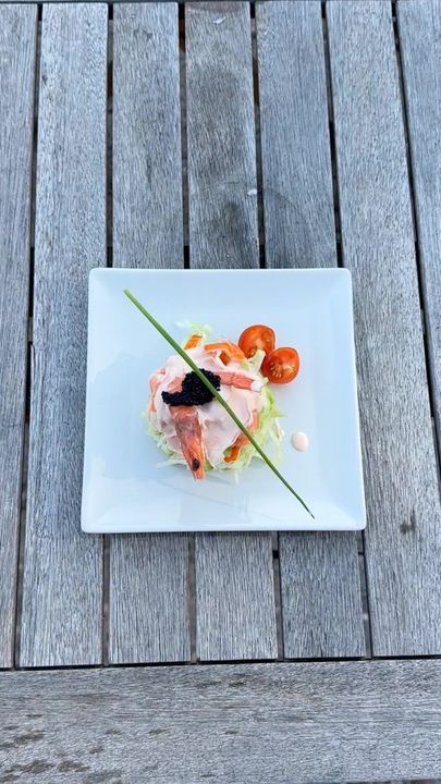 Un plato blanco cubierto con camarones y tomates sobre una mesa de madera.