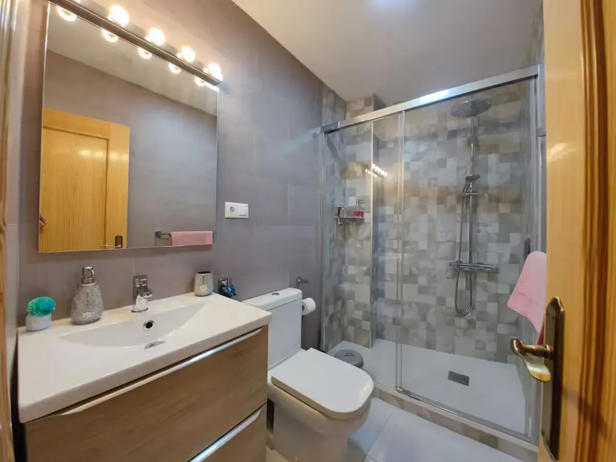 Baño con paredes grises, ducha de cristal, tocador y sanitario.