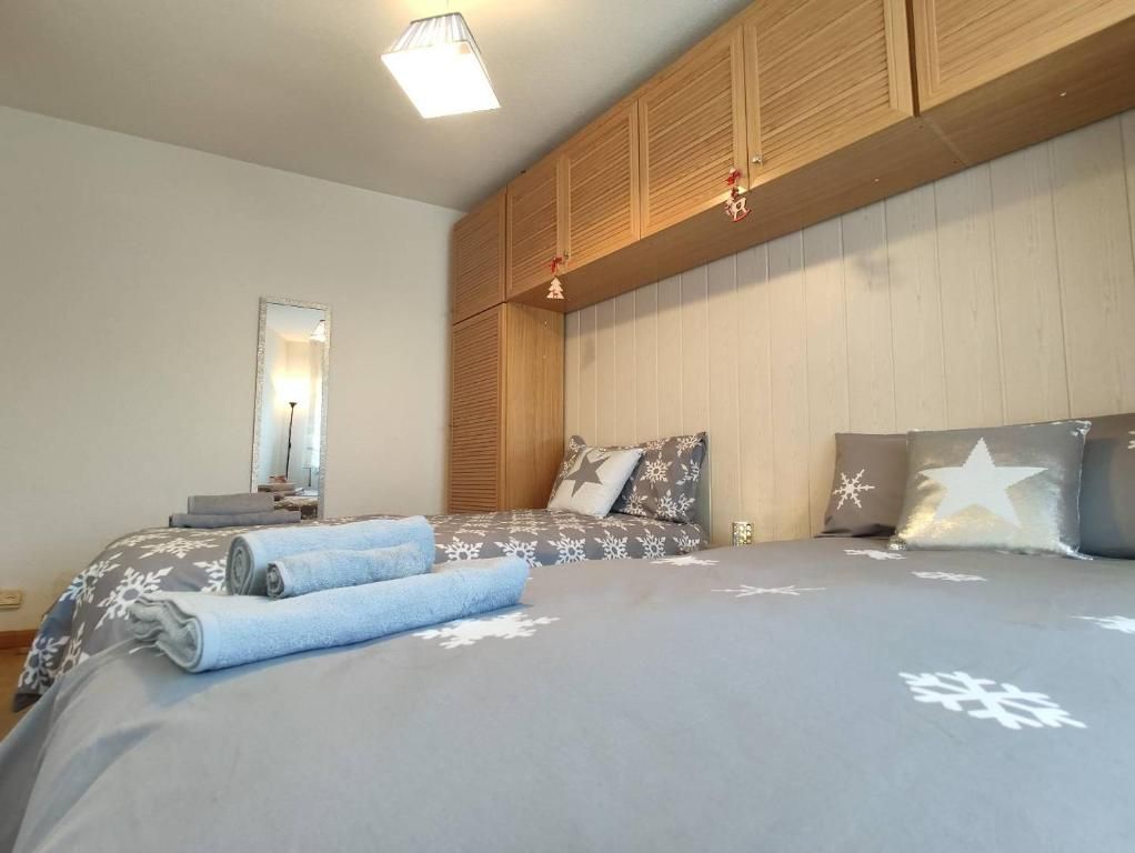 Dormitorio con dos camas cubiertas con ropa de cama gris con estampado de copos de nieve y armarios de madera de color claro encima.