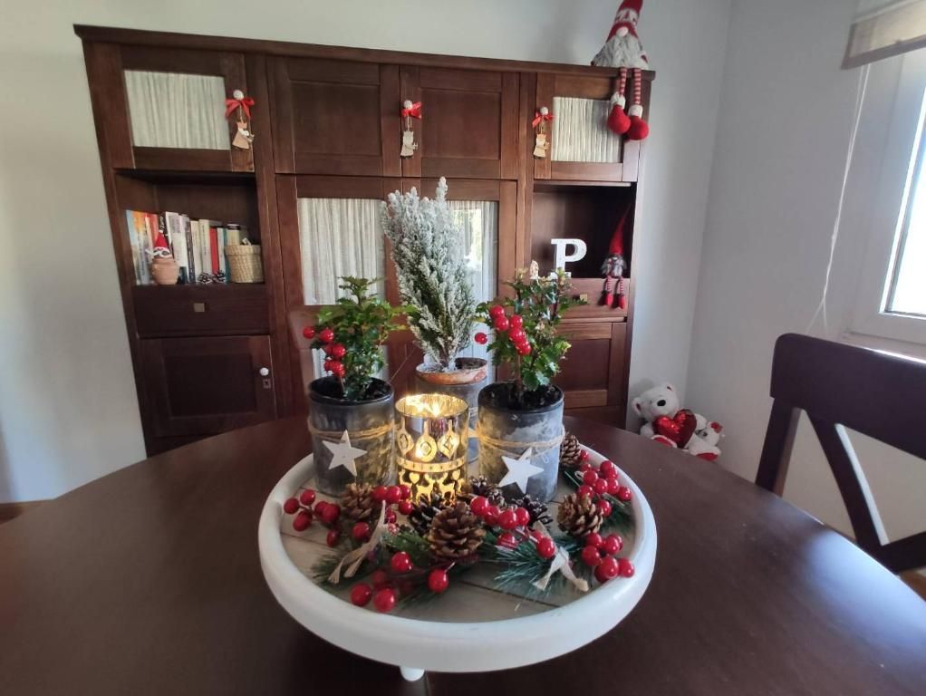 Centro de mesa navideño con plantas, velas, bayas y adornos. Al fondo, un armario de madera.