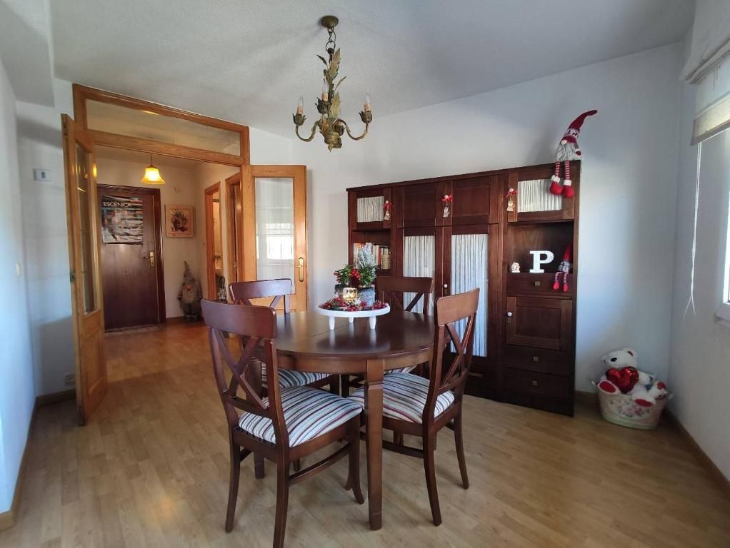 Comedor con mesa de madera, sillas y armario de madera oscura. Una puerta da a otra habitación.