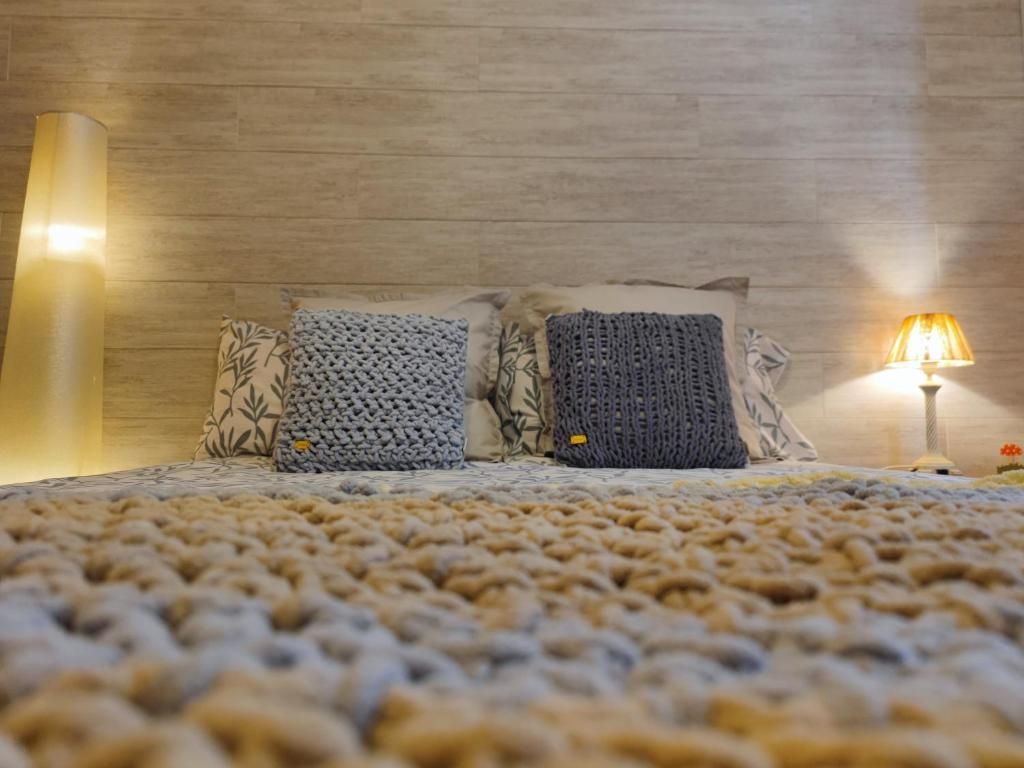 Acogedor dormitorio con cama, manta de punto, almohadas y lámparas; colores neutros.