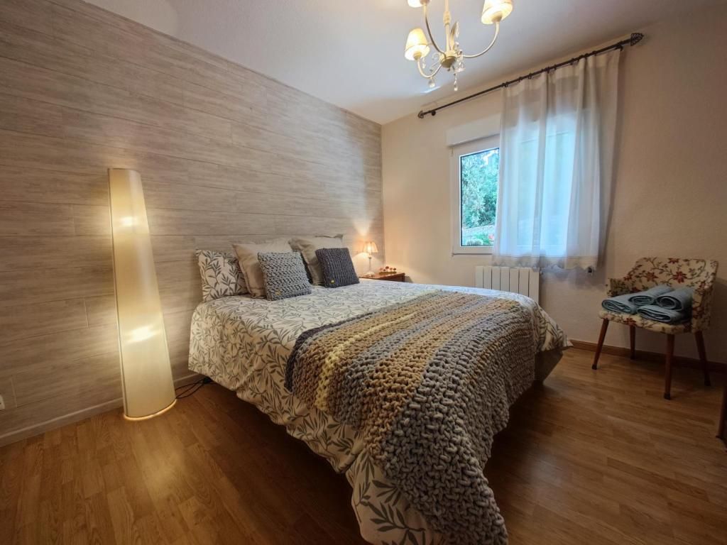 Dormitorio con cama, ropa de cama estampada, suelo de madera, lámpara de pie alta y ventana.