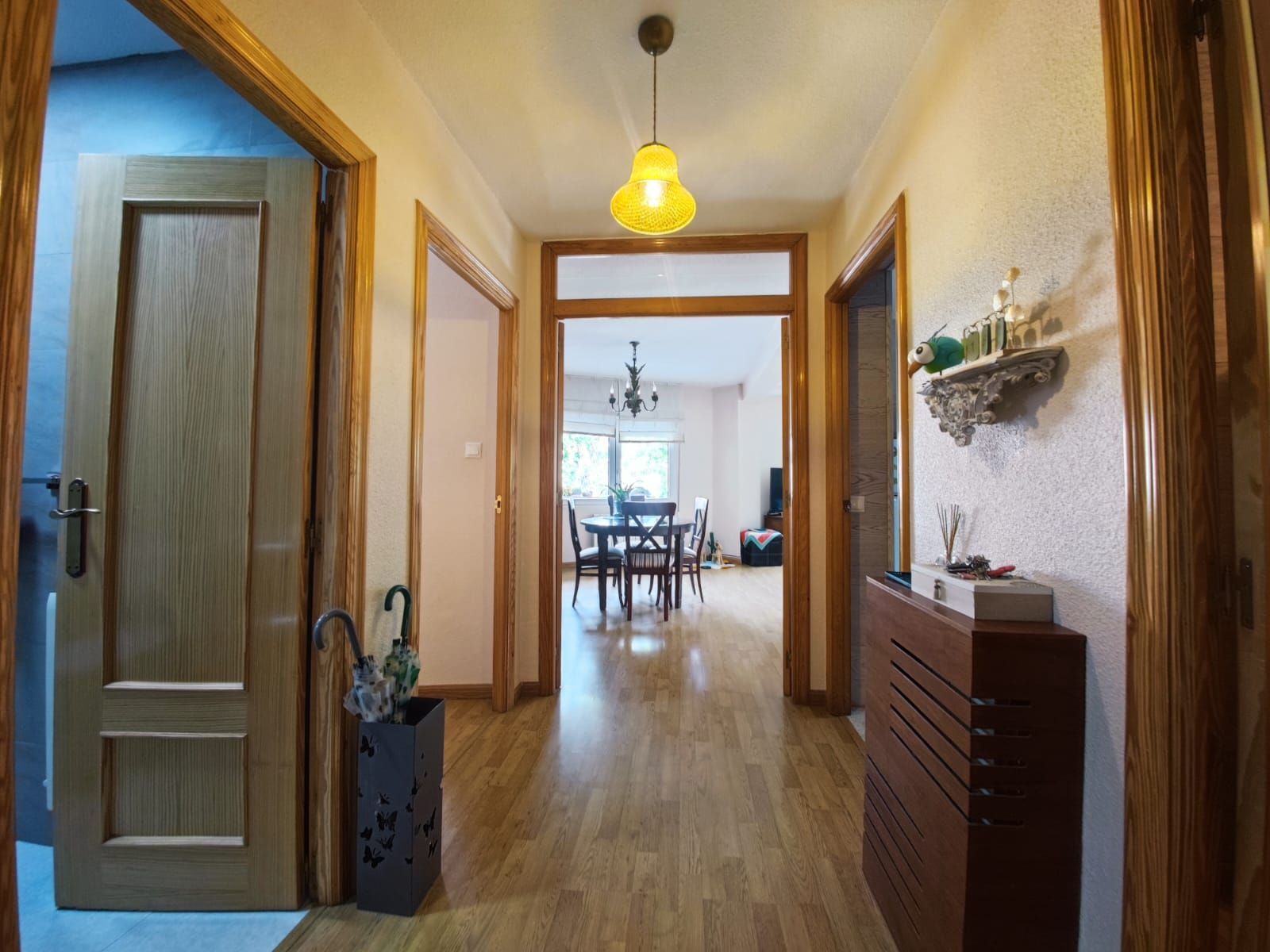 Pasillo con puertas y suelos de madera, con vista a un comedor con mesa y sillas.