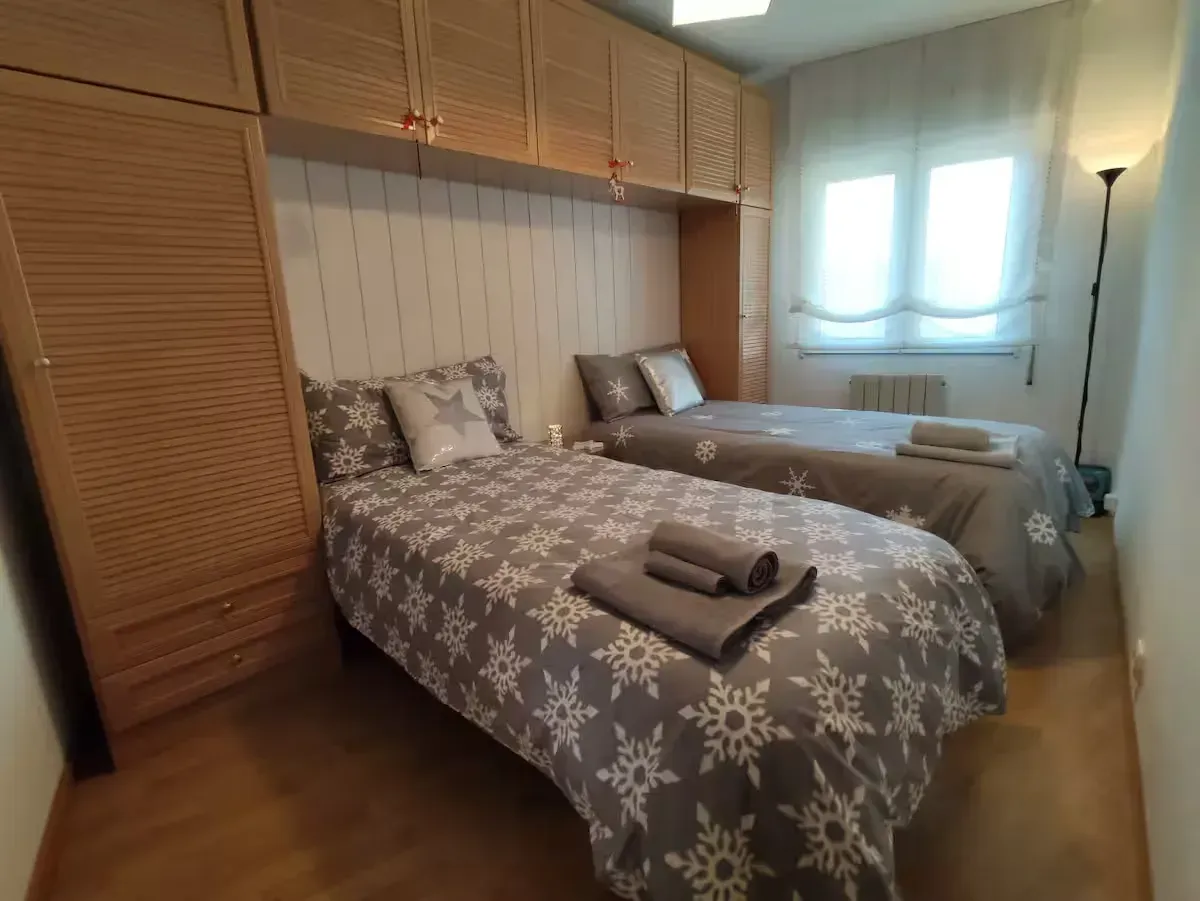 Camas individuales en un dormitorio con ropa de cama con estampado de copos de nieve, armarios de madera y una ventana. 