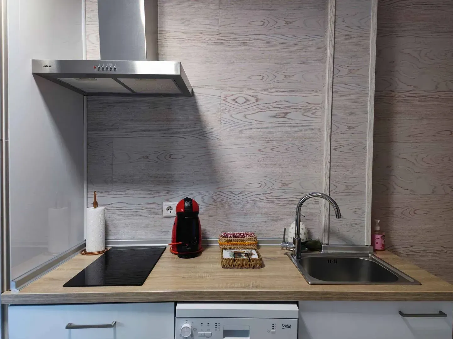 Encimera de cocina con electrodomésticos integrados y campana extractora; salpicadero y encimera de madera clara.