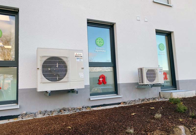 Klimaanlagen, die außerhalb eines Gebäudes mit Fenstern mit Apothekenlogo montiert sind.