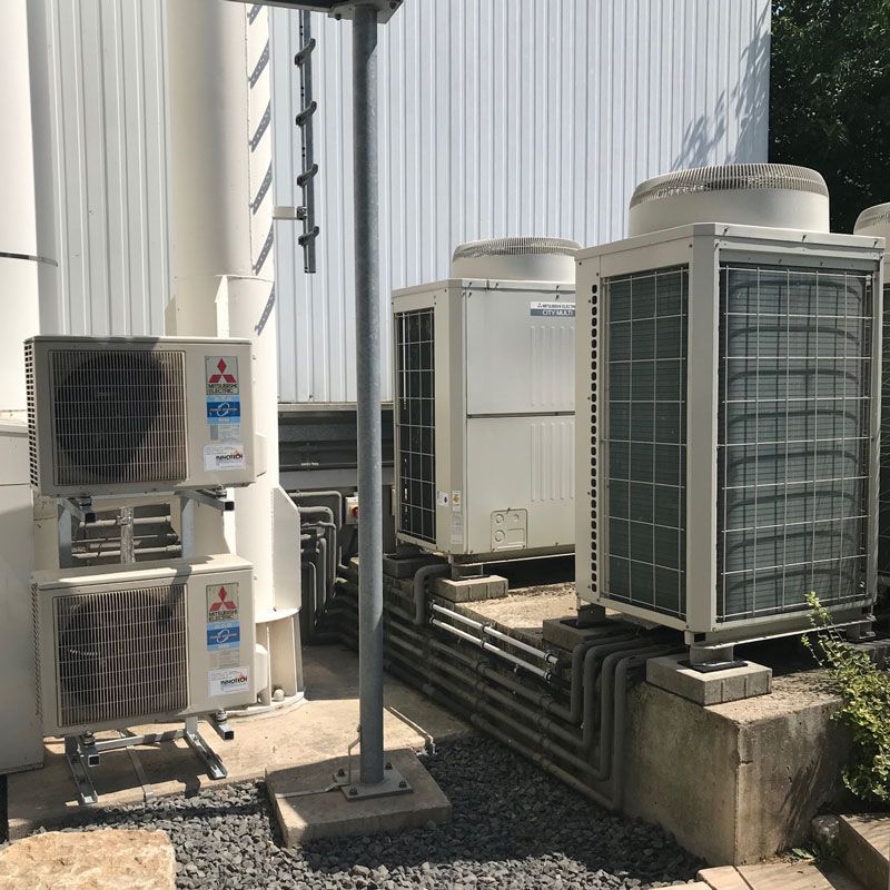 Außenklimaanlagen vor einem weißen Gebäude, in der Nähe eine Stange und eine Leiter.