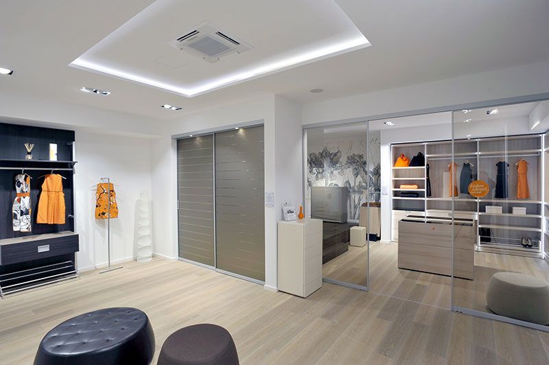 Moderner begehbarer Kleiderschrank mit Kleiderständern, Schubladen und Sitzgelegenheiten. Helle Holzböden, Glaswände und neutrale Farben.