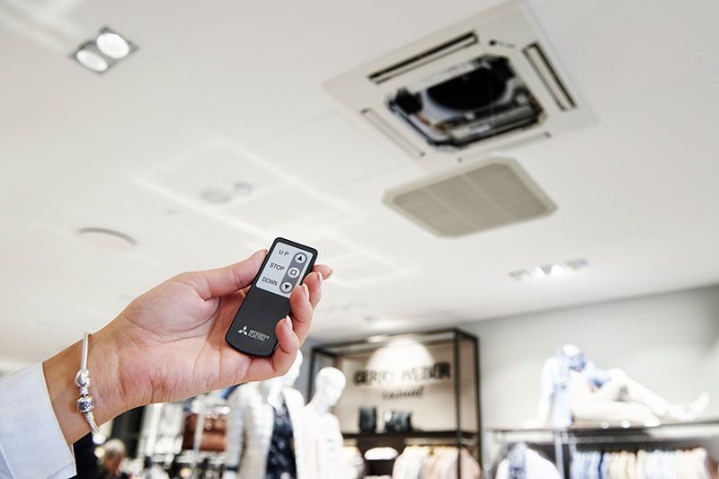 Hand hält Fernbedienung und zeigt auf an der Decke montierte Klimaanlage im Einzelhandelsgeschäft.