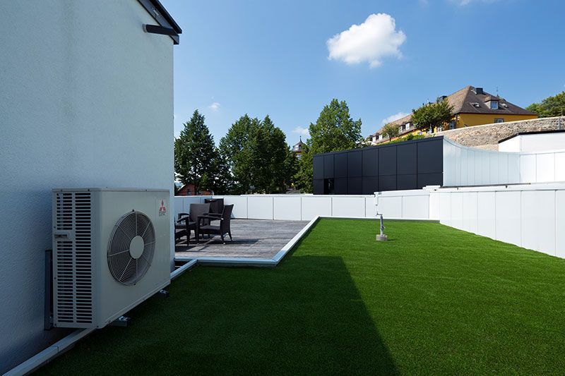 Außenbereich mit Klimaanlage, Kunstrasen und Sitzgelegenheiten im Freien unter strahlend blauem Himmel.