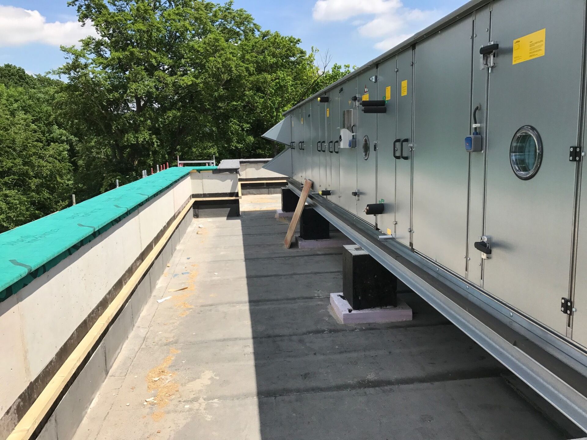 HVAC-Dacheinheit auf einem grauen Flachdach, schwarze Stützen, Bäume im Hintergrund.