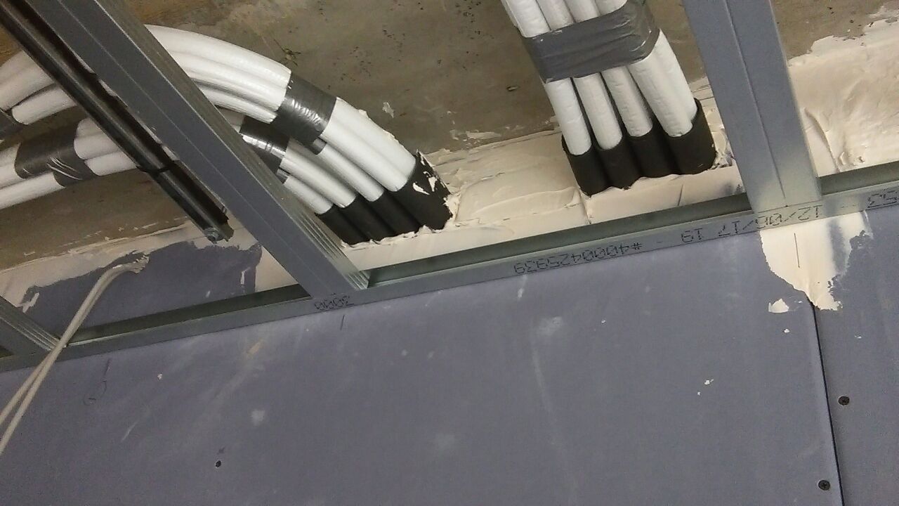 Grauer Metallrahmen mit weißen Leitungen, die mit schwarzem Klebeband an einer Betondecke in der Nähe einer grauen Wand befestigt sind.