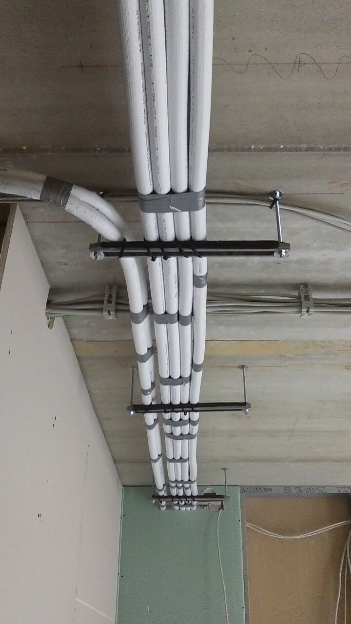 Weiße isolierte Rohre, die mit Metallklammern an einer Betondecke in einer Baustelle befestigt sind.