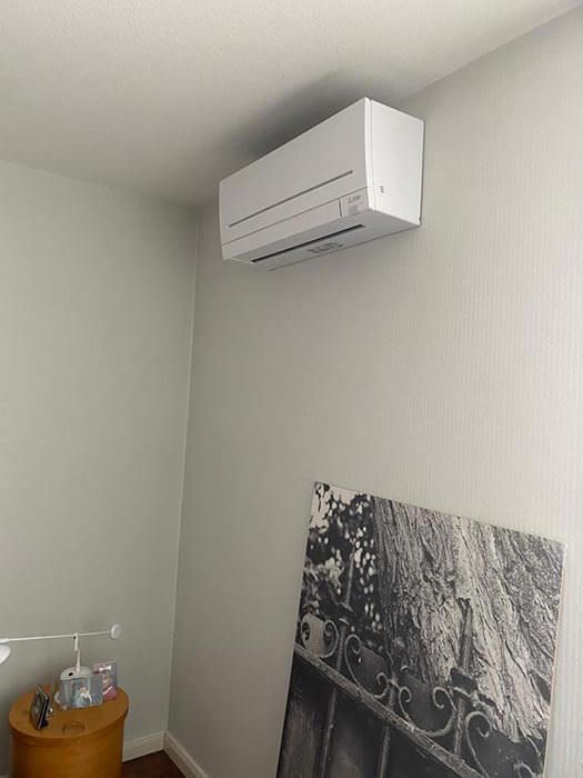 Weiße, an der Wand montierte Klimaanlage an einer hellgrünen Wand über einem Schwarzweißfoto.