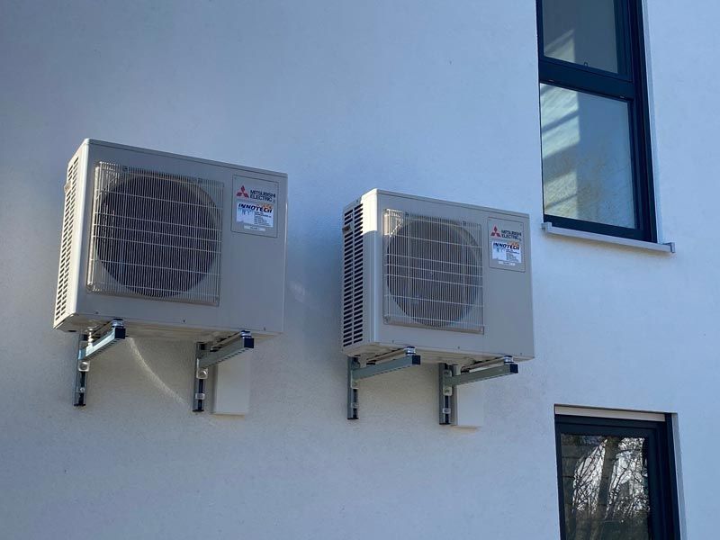 Zwei beige Klimaanlagen, die an der Außenseite eines weißen Gebäudes montiert sind.