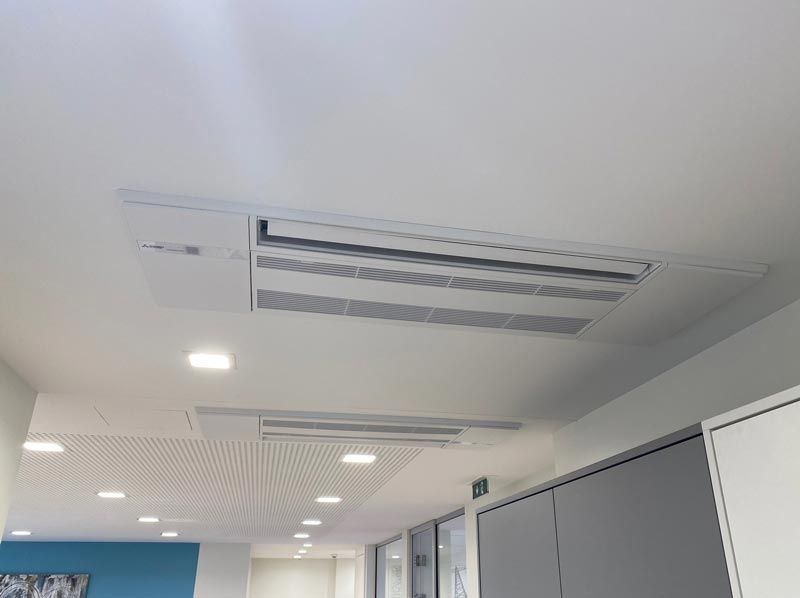An der Decke montierte Klimaanlagen in einem weißen Büro mit Einbauleuchten.