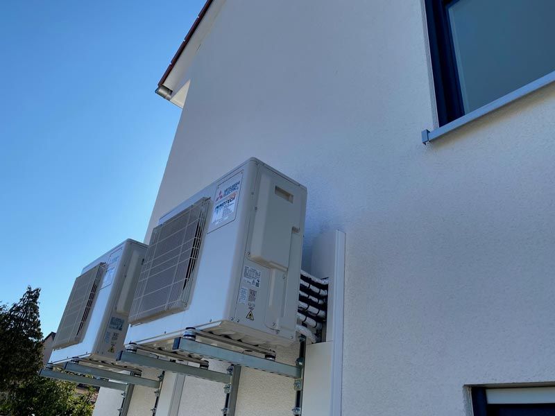 Zwei weiße Klimaanlagen, montiert an einer weißen Gebäudewand, vor dem Hintergrund eines blauen Himmels.