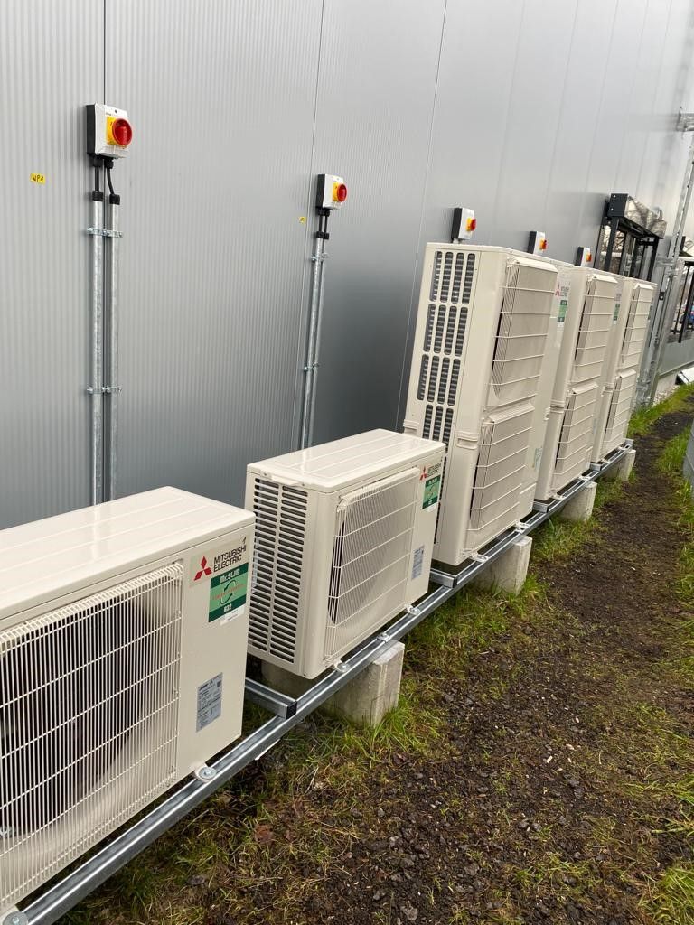 Reihe von Klimaanlagen, die auf einem Metallrahmen vor einem grauen Gebäude montiert sind.