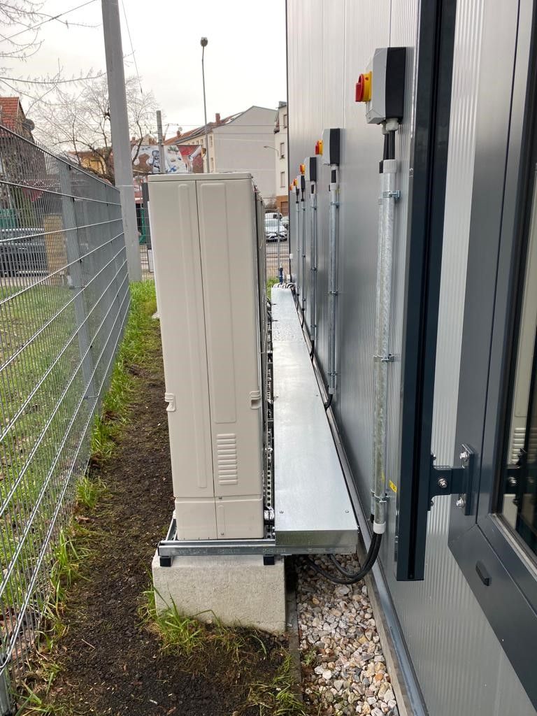 Elektrische Geräte im Außenbereich neben einem Gebäude und Zaun montiert.