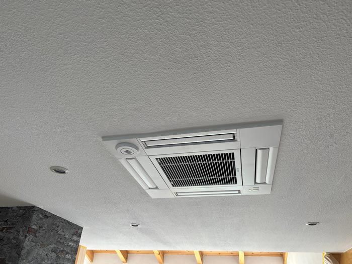 An der Decke montierte Klimaanlage mit weißem Rahmen an einer strukturierten weißen Decke.