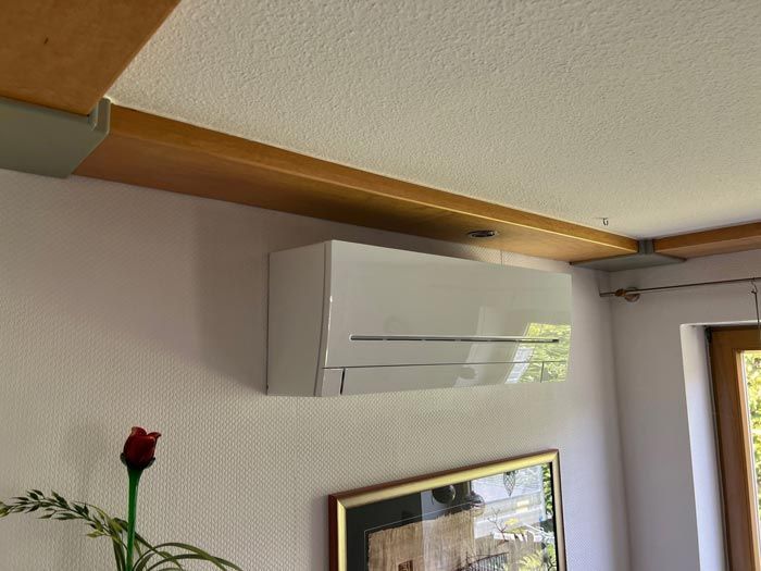 Weiße Klimaanlage an einer strukturierten Wand, unter einem Holzbalken.