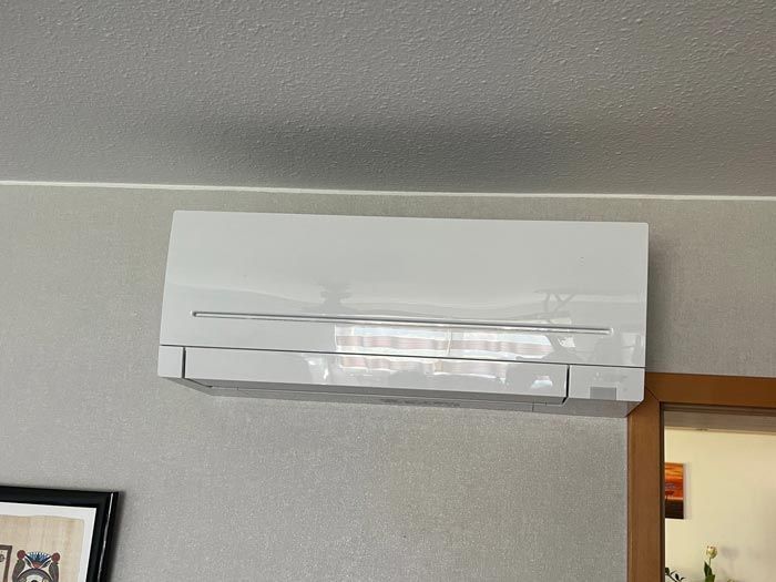 Weiße, kanallose Klimaanlage, an einer grauen Wand über einem Türrahmen montiert.