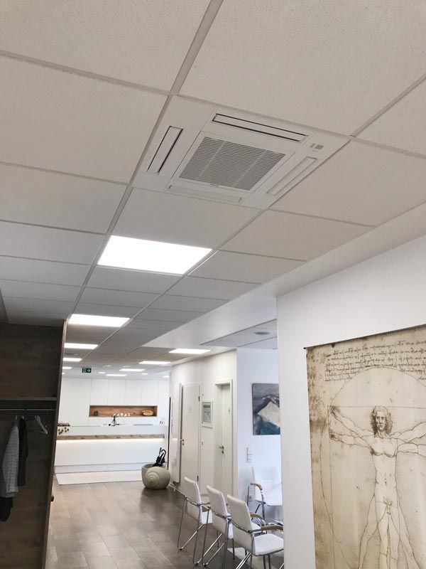 An der Decke montierte Klimaanlage in einem modernen Büro. Inklusive quadratischer Lampen und einem Flur mit Stühlen und Kunstwerken.