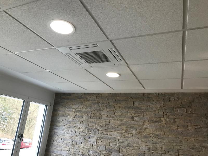 Deckenplatten mit Einbauleuchten und einer zentralen Lüftungsöffnung über einer Steinmauer.