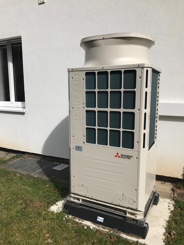 Große beige Mitsubishi-Wärmepumpe außerhalb eines Gebäudes auf einer Betonplatte.