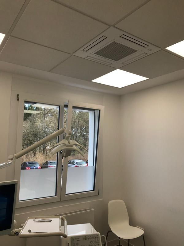 Innenraum einer Zahnarztpraxis mit Fenster, Zahnarztstuhl und Deckenbeleuchtung.