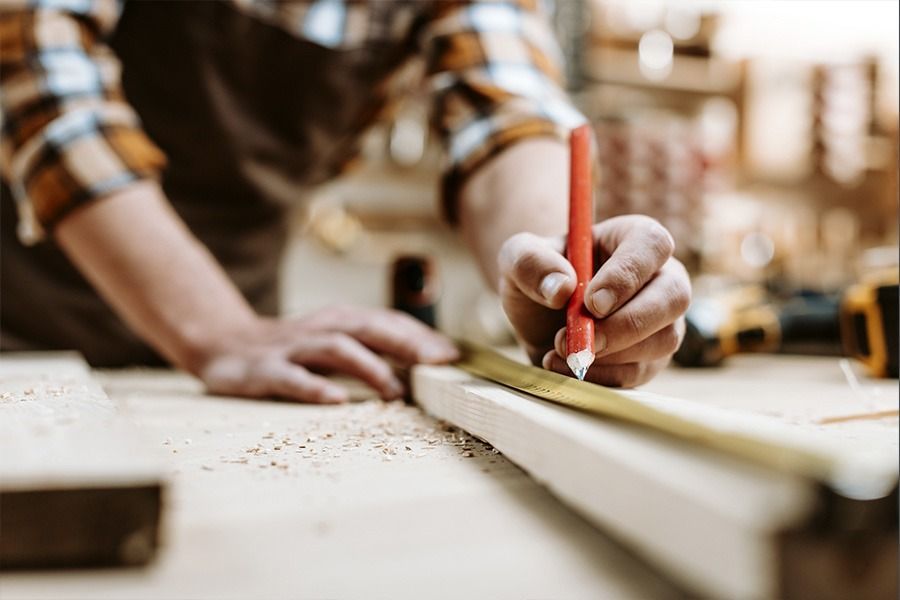 Un hombre está midiendo un trozo de madera con una cinta métrica y un lápiz.