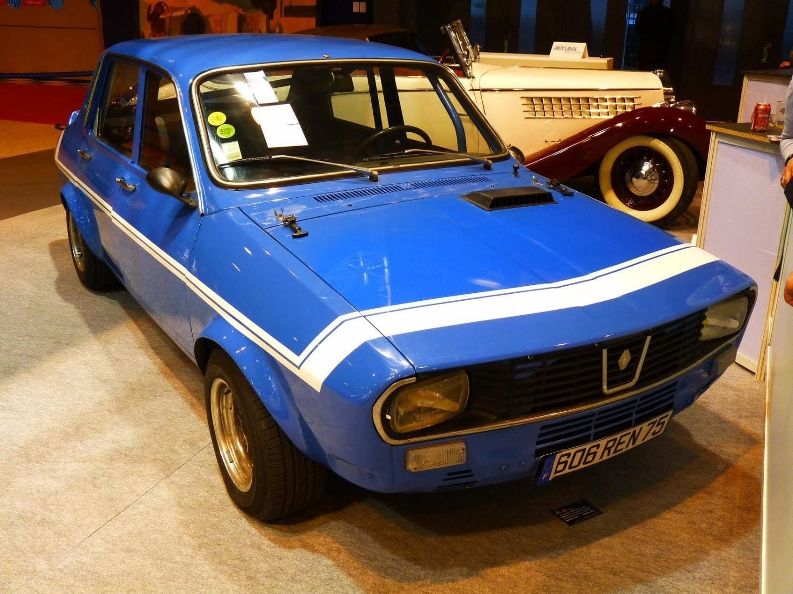 Coche clásico azul con franjas de carreras blancas exhibido en un evento.