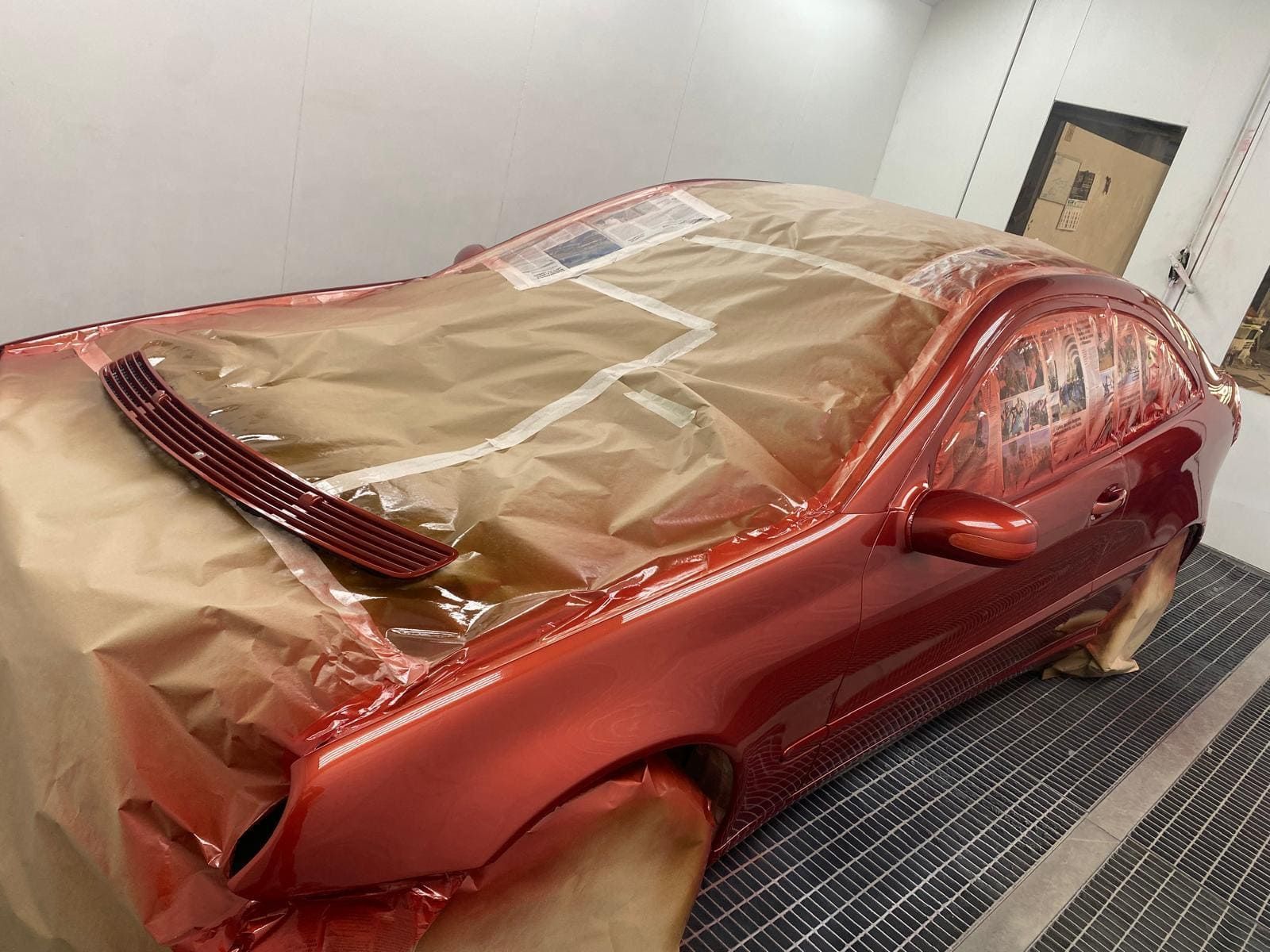 Coche en cabina de pintura, parcialmente enmascarado, siendo pintado de color rojo metalizado.