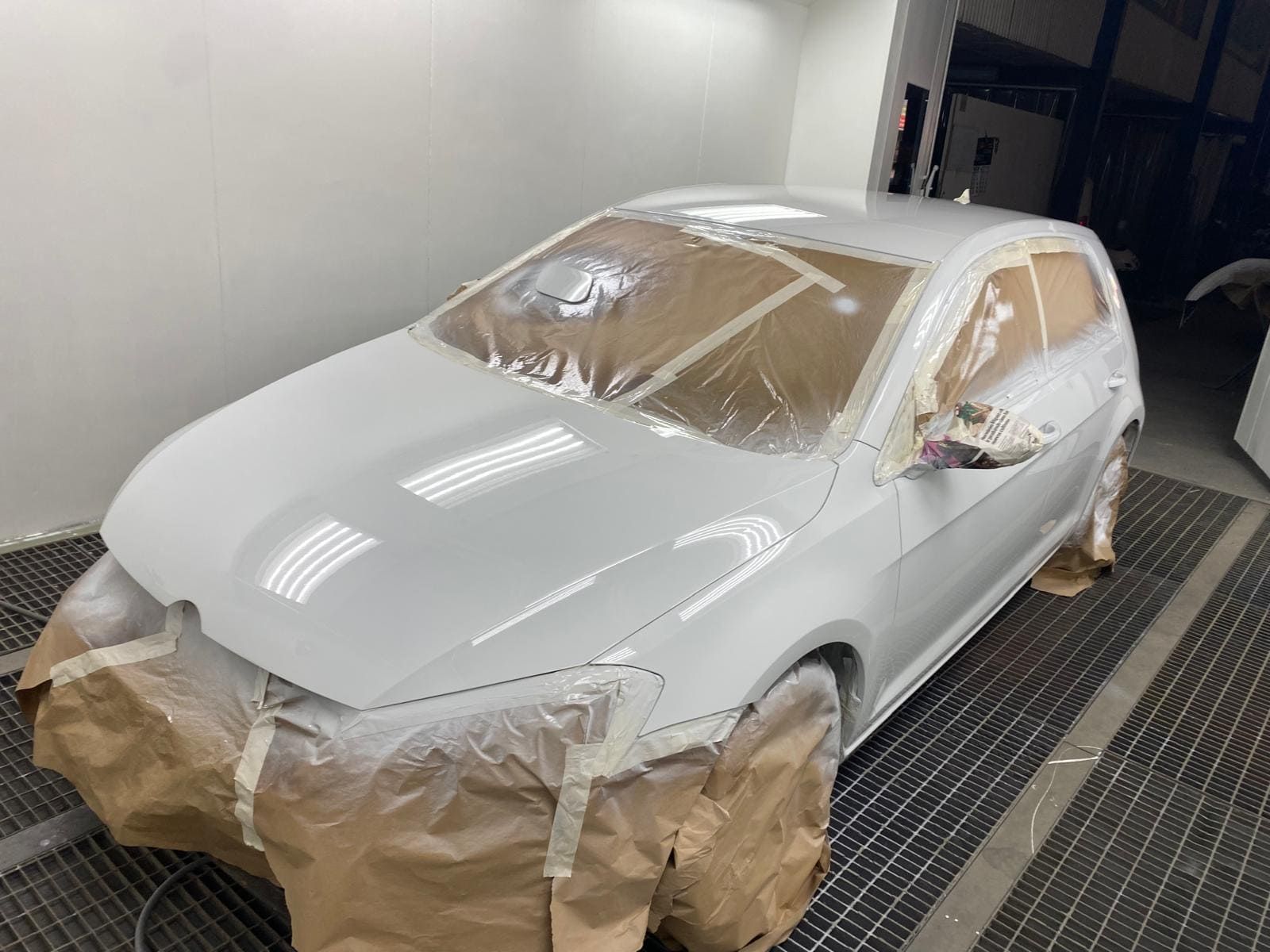 Coche blanco siendo pintado en un taller de carrocería, enmascarado para su protección.