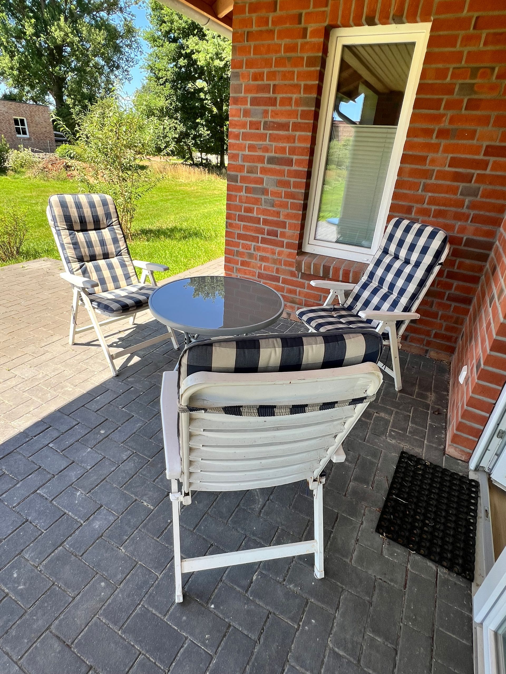 Terrasse mit weißen Stühlen, kleinem Tisch und Backsteingebäude mit Fenster.