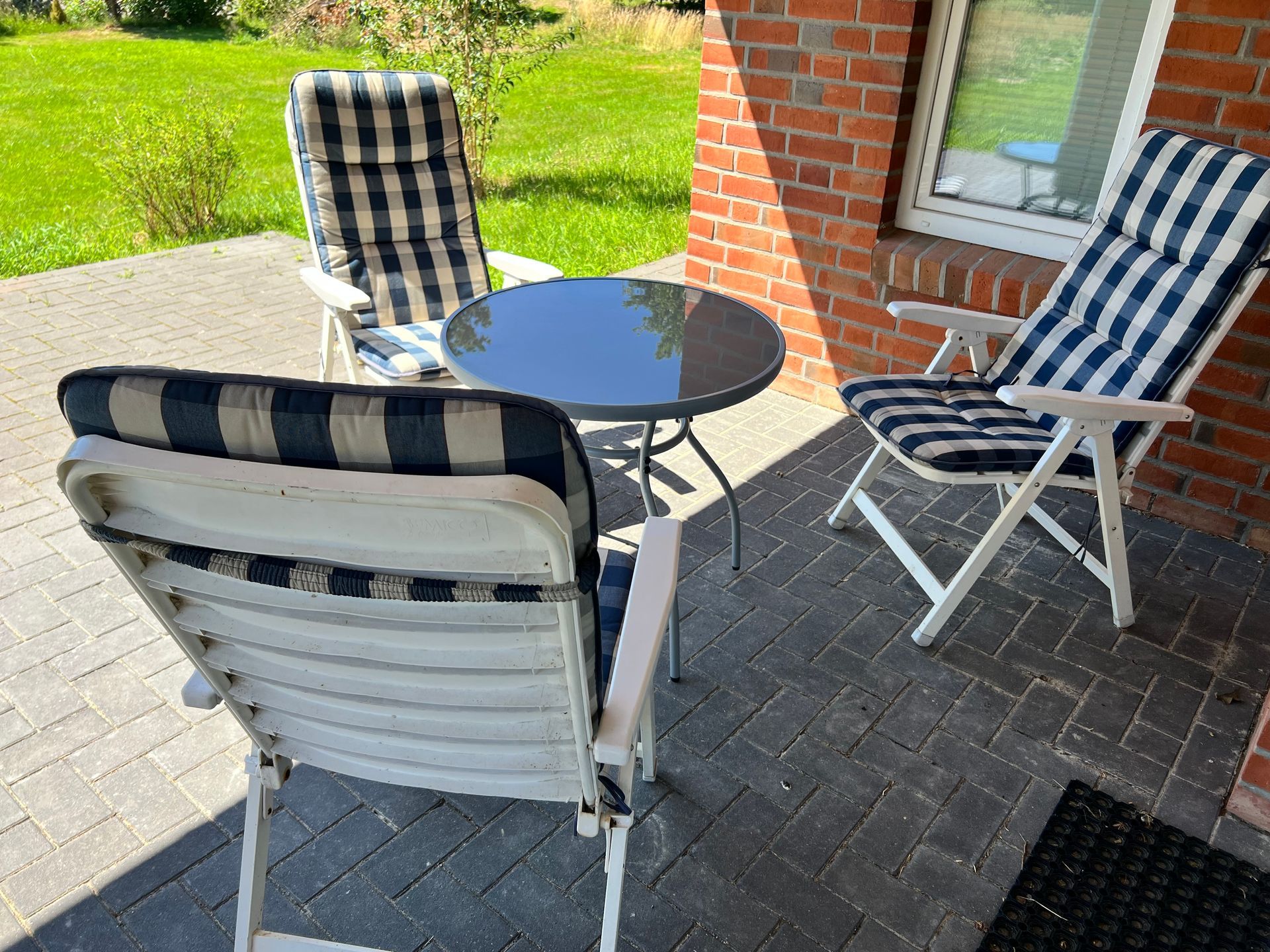 Terrasse mit drei gestreiften Stühlen und einem kleinen runden Tisch auf einem Backsteinpflaster.