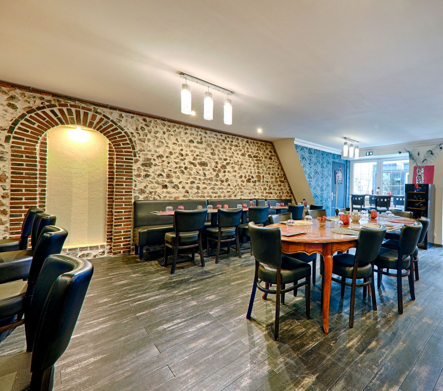 Intérieur du restaurant avec tables dressées pour le service, murs en pierre et sièges noirs.