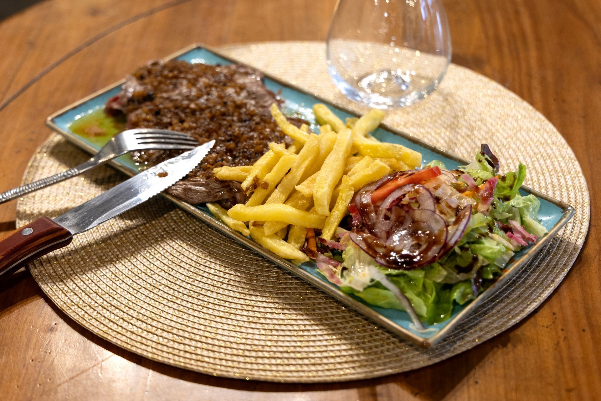 Steak accompagné de frites et de salade sur une assiette rectangulaire, avec un couteau, une fourchette et un verre d'eau.