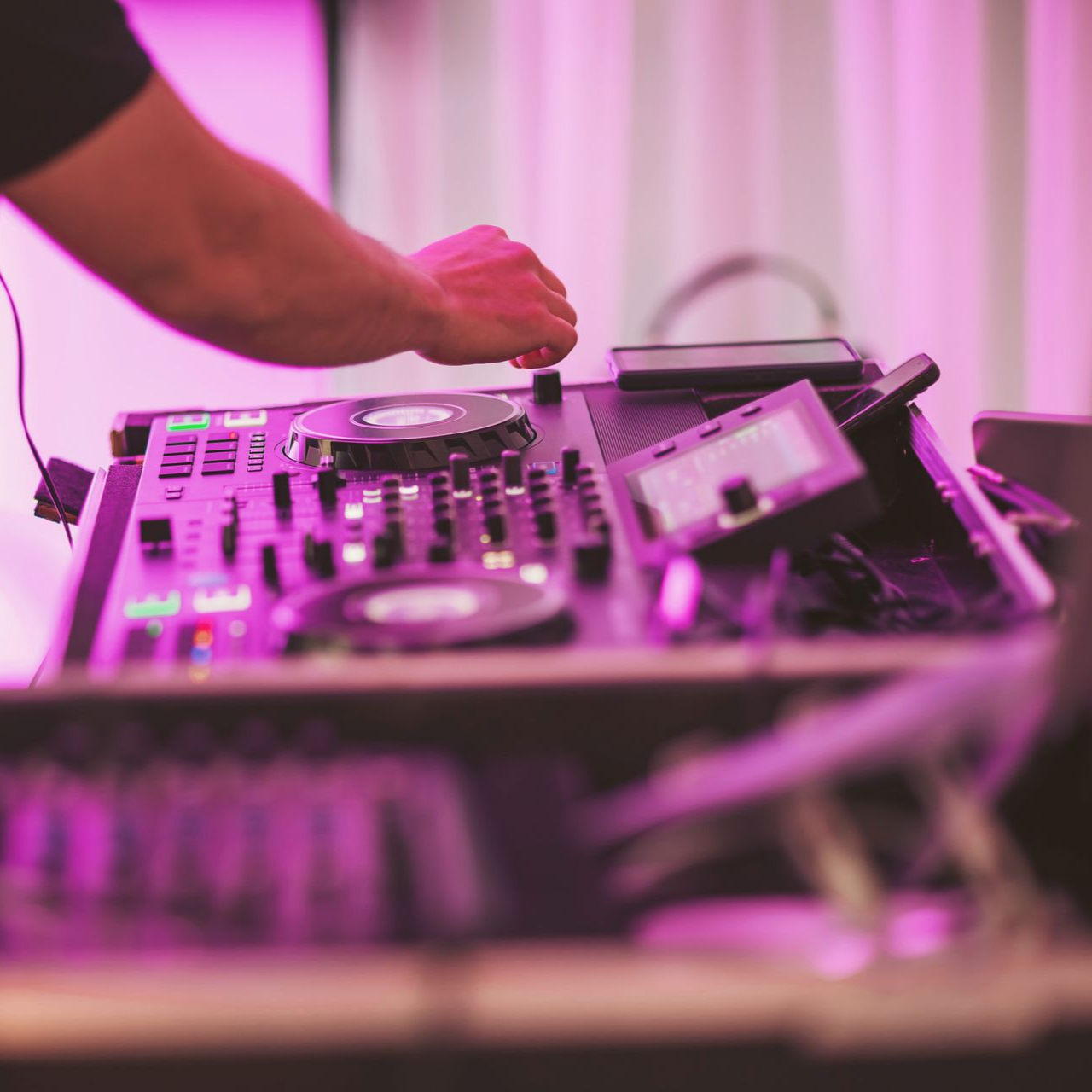 Un DJ mixe de la musique sur une console éclairée par une lumière rose.