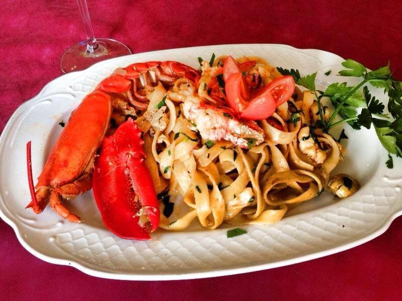 Un plato de pasta con langosta y tomates encima.
